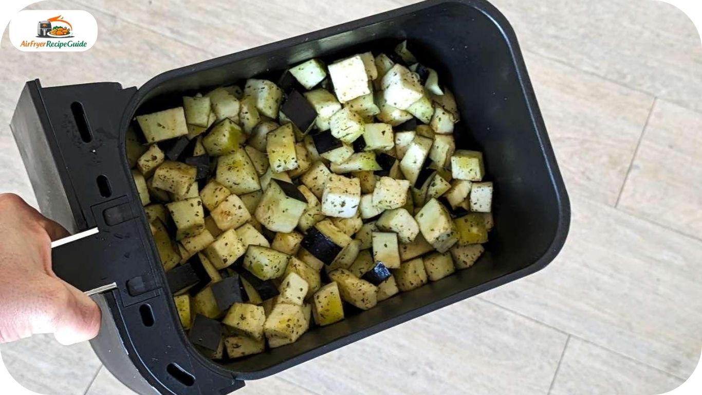 Seasoned eggplant cubes arranged in an air fryer basket before cooking