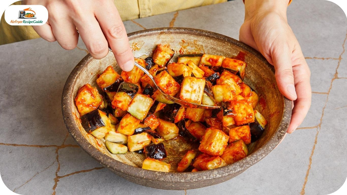 Eggplant cubes being tossed with spices in a mixing bowl